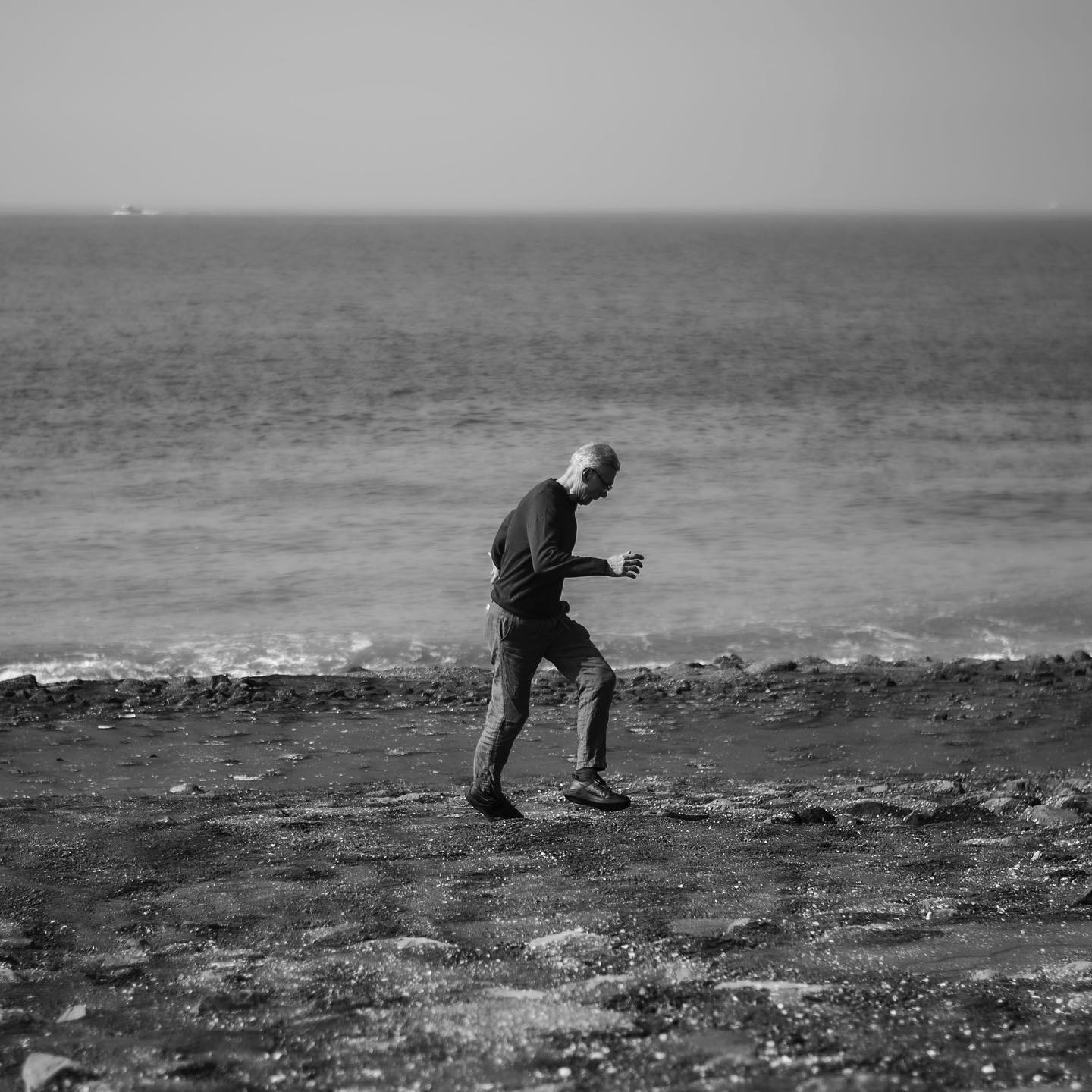 Iemand loopt langs de zee in Zeeland, in zwart-wit